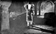 Black and white piece of a girl with an elephant head standing in castle room with crumbling archways.  Deliberately blurry and with scratches outlining the figure.